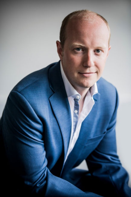 Steve Holloway poses sitting for a photo in a suit