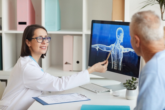 Female doctor showing an older patient a 3D skeleton model on a computer screen....