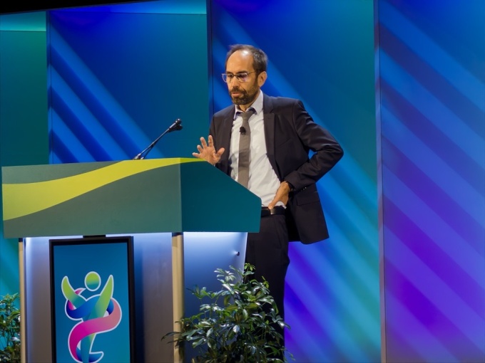 Man – Alexander Drzezga – standing on a stage while giving a presentation...