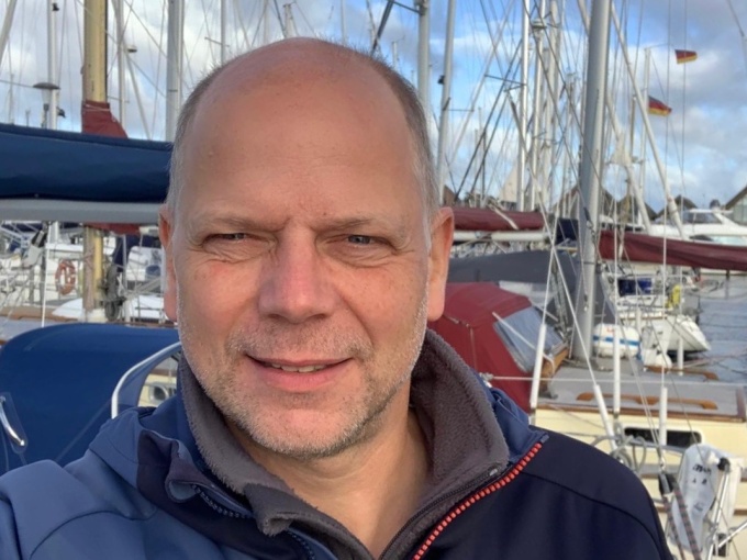 Man at the front looking directly at the camera with ships in the background...