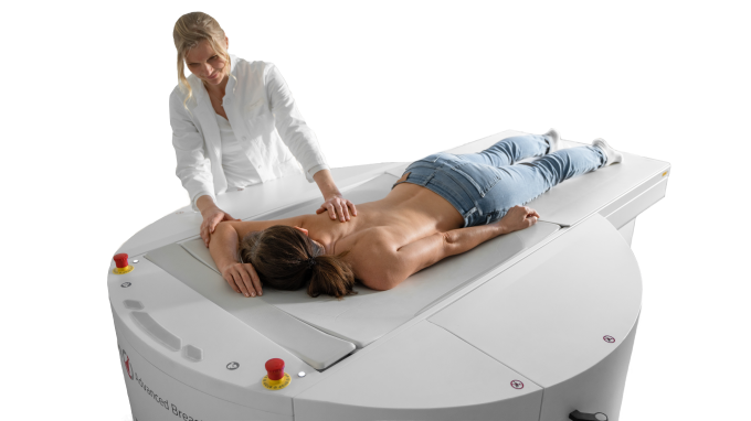 Woman lying down for a breast CT while a medical professional stands next to...