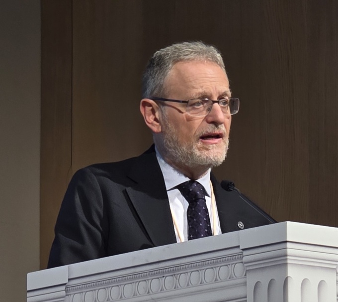 Man talking on a stage while standing behind a podium: Andrea Rossi...