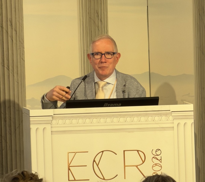 Man speaking into a microphone behind a speaker podium: Adrian Brady...