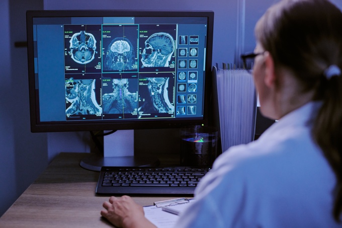 Woman sitting at a desk and looking at medical scans disyplayed on a monitor in...