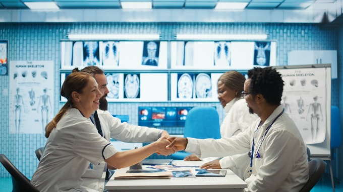 Group of medical professionals sitting around a desk shaking hands...