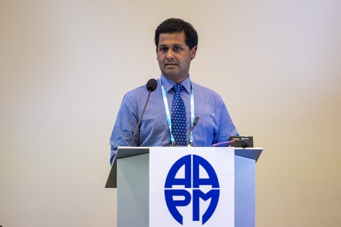 Man in a blue shirt talking on a stage while standing behind a podium: Anshuman...