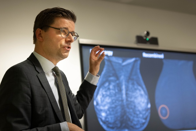 Man in a suit talking next to a screen showing breast imaging...